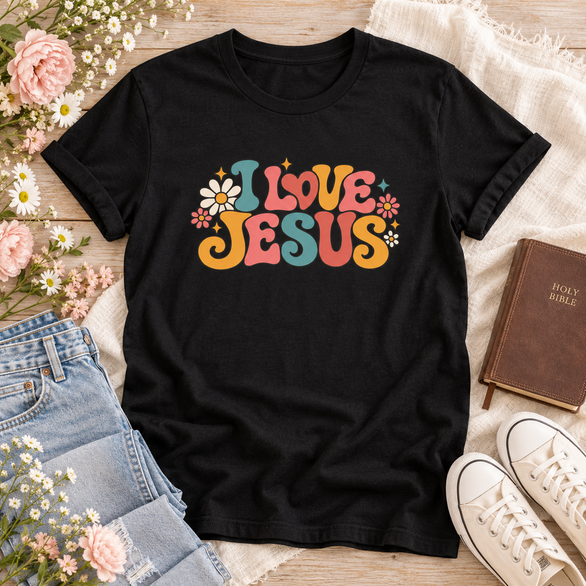 Black T-shirt reading “I Love Jesus” in colorful retro lettering, surrounded by daisies, small flowers, and sparkle accents.