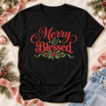 A black short-sleeve T-shirt laid flat with a festive 'Merry & Blessed' holiday graphic in red, green, and white. 