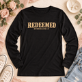 Black Redeemed long-sleeve tee with gold lettering and Ephesians 1:7, shown in a styled flat lay.