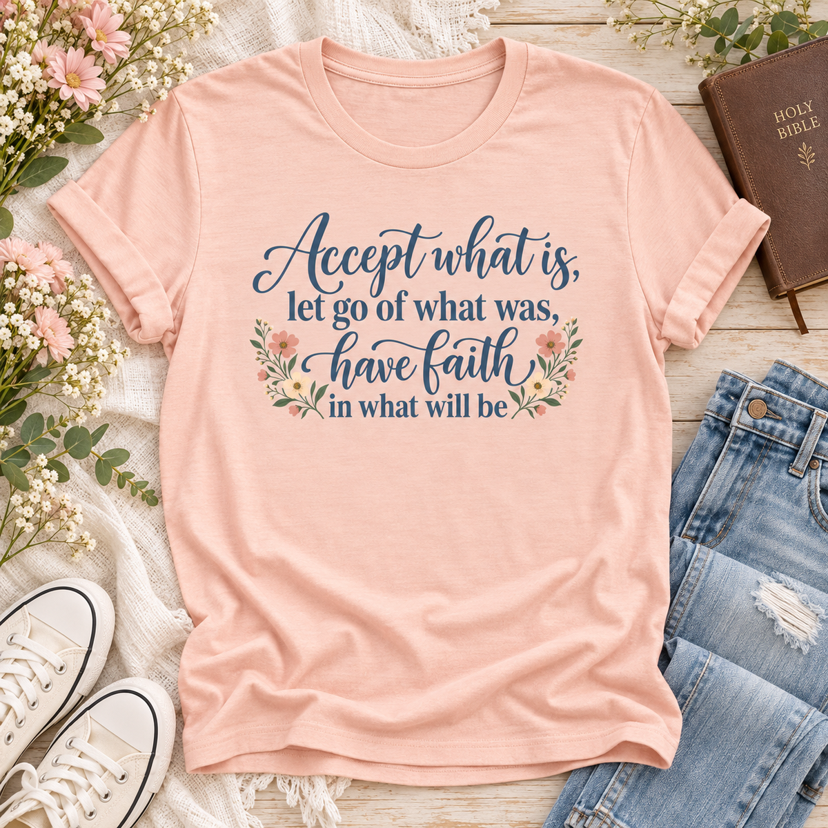 Peach T-shirt reading “Accept what is, let go of what was, have faith in what will be,” in dark blue lettering with floral accents.