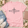 Pink Waymaker Christian T-shirt featuring distressed dark lettering across a brushstroke-style cross with mountain outlines.