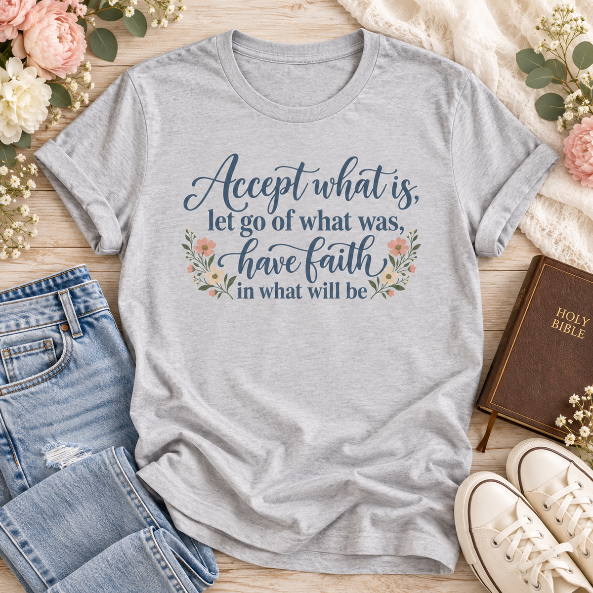 Silver T-shirt reading “Accept what is, let go of what was, have faith in what will be,” in dark blue lettering with floral accents.